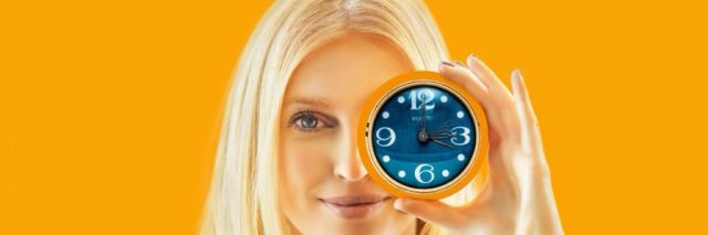 Woman holding a clock near her left eye, symbolizing the importance of time and the effectiveness of Anahata Body Care Products in achieving timely skincare results."